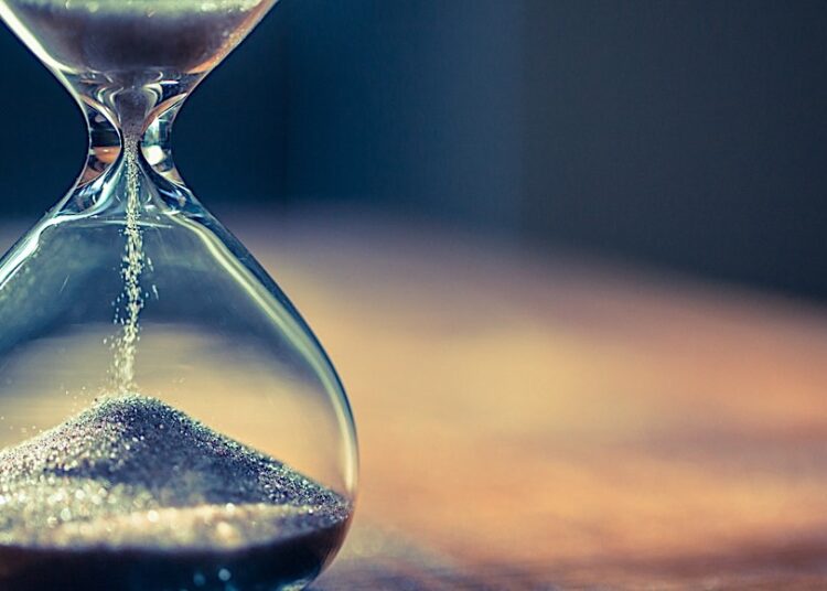 Sand running through the bulbs of an hourglass measuring the passing time in a countdown to a deadline, on a dark background with copy space.