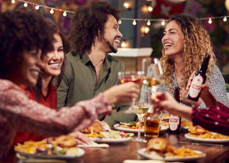 Multi-Cultural Group Of Friends Enjoying Night Out Eating Meal And Drinking In Restaurant Together
